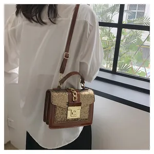 Detail of a dark brown crossbody bag with gold glitter finish and metal chain handle