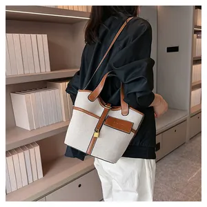 Detail of canvas bucket bag with leather trim and gold lock worn by a model