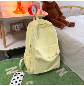Detail of light yellow canvas backpack featuring bear logo patch and zippered front pocket