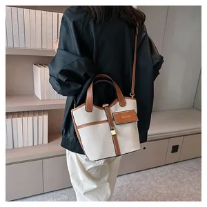 Detail of the canvas bucket bag showing brown leather strap and golden padlock charm
