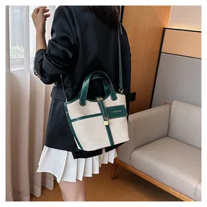 Detail of canvas bucket bag with green leather trim and gold padlock on a model