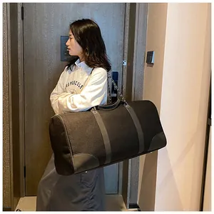 Large black canvas travel tote bag with silver chain straps shown in hotel scene