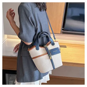 Side view of beige canvas bucket bag with navy leather trim and gold buckle worn by model