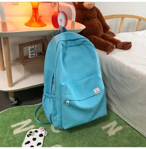 Detail view of light blue canvas backpack featuring a pink cartoon bear label and side pocket