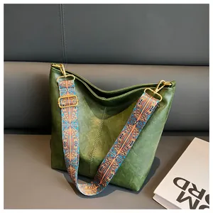 Detail of dark green textured hobo bag with a colorful ethnic style wide guitar strap