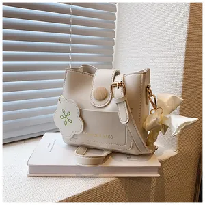Détail du sac seau crème avec bouton en bois, foulard en soie et breloque florale