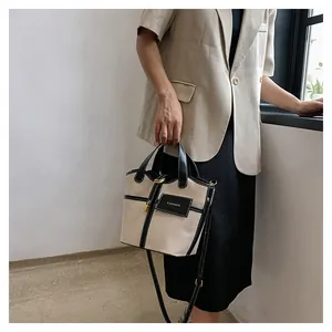 Detail of canvas bucket bag with black leather trim and contrast stitching on a model