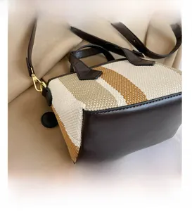 Detail shot of the woven canvas bag with brown leather base and golden hardware