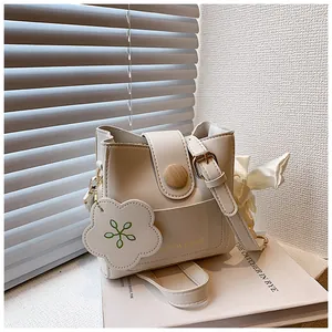 Détail du sac seau beige avec boucle en bois et breloque fleurie sur un livre