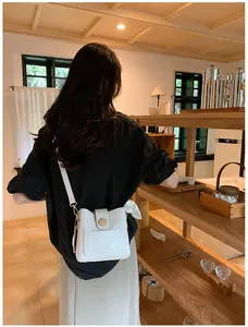 Détail d'un sac seau blanc avec garniture dorée et nœud latéral sur un mannequin
