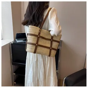 Detail of straw tote bag showing woven texture, brown leather straps, and gold rivets