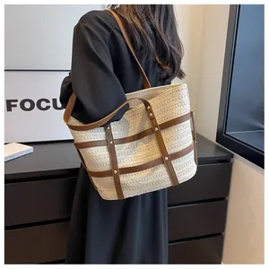 Detail of straw tote bag featuring white woven texture, brown leather straps and gold rivets