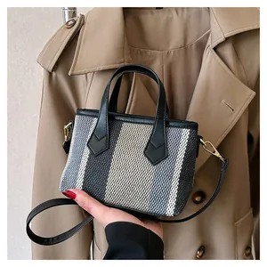 Detailed close-up of striped canvas tote bag with black leather handles and gold hardware