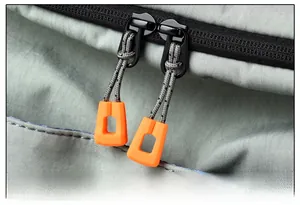 Macro shot of a grey nylon backpack with a high-contrast bright orange zipper puller