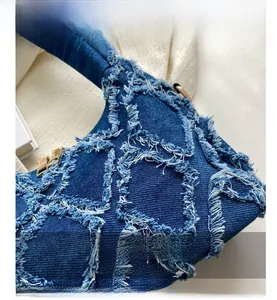 Close-up of distressed blue denim handbag showing frayed edges and golden hardware detail