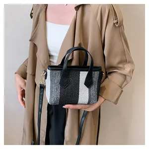 Detail of striped canvas tote with black leather handles and woven texture on model