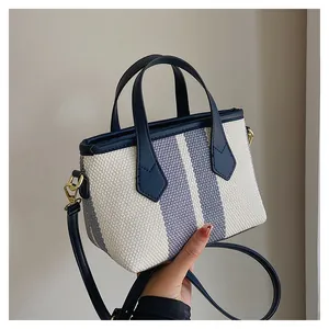 Close-up of striped canvas bucket bag showing navy leather trim and gold hardware detail
