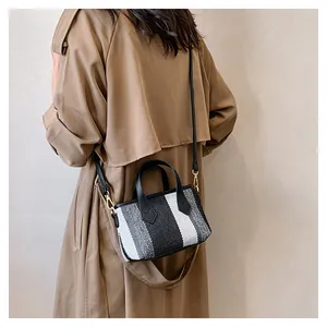 Detail of striped canvas handbag with gold hardware on a camel-colored trench coat