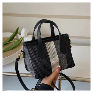 Detailed view of woven striped bucket bag with black leather handle and gold hardware