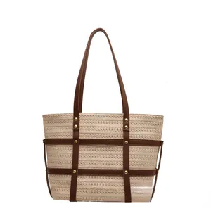 Minimalist straw tote bag with brown leather trim and golden rivets on white background