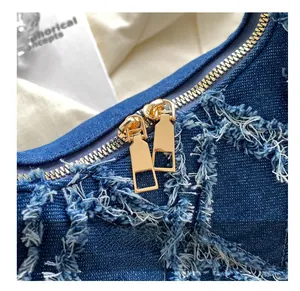 Detail of dark blue denim handbag featuring gold double zippers and frayed fringe texture