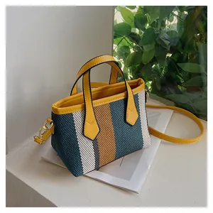 Detail of striped woven bucket bag with yellow leather handles and golden metal hooks