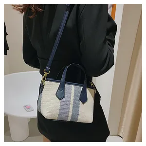 Detail view of canvas striped bucket bag with blue leather straps on a model