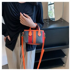 Detailed shot of striped canvas handbag with orange leather trim and golden metal hardware