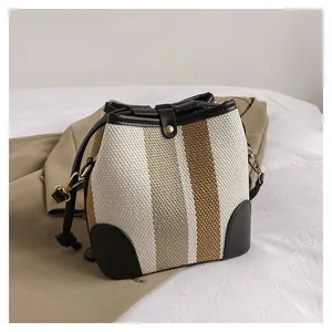 Detail of striped woven bucket bag featuring brown leather trim and metallic gold hardware