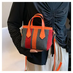 Detail of woven striped crossbody bag in orange, red and gray with leather handle
