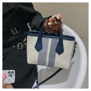 Detail of canvas mini bucket bag with blue vertical stripes and navy leather trim handles
