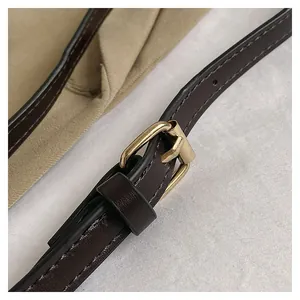 Detail of dark brown leather strap with adjustable gold metal buckle on canvas bucket bag