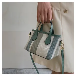 Detail of striped canvas mini bucket bag with green leather handles and gold metal clips