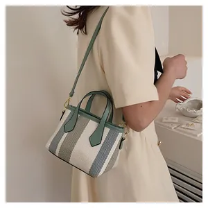 Close-up of a striped canvas bucket bag with green leather handles and detachable strap