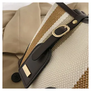 Detail of woven bucket bag featuring cream texture, brown leather trim, and gold hardware