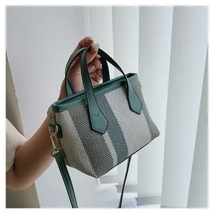 Detail of striped woven bucket bag with green faux leather handles and gold metal rings