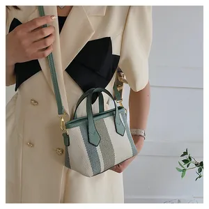 Detail of striped canvas mini bucket bag featuring green leather trim and golden hardware
