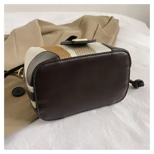 Detail of striped woven bucket bag with brown leather trim and golden metal buckle clasp