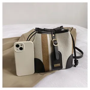Detail view of striped woven bucket bag with leather strap and metal buckle accent