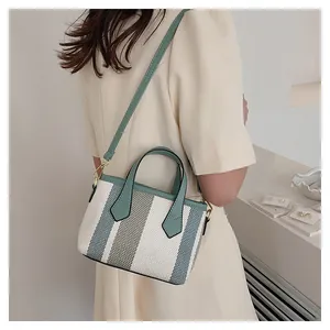 Detail view of a striped canvas bucket bag with green leather trim and gold hardware