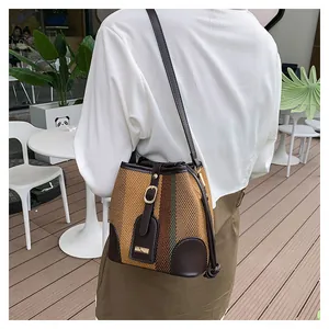 Detail of woven striped bucket bag featuring brown leather trim and gold metal hardware