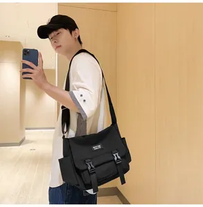 Détail du sac messager en toile noire avec boucles en plastique et large bandoulière en nylon