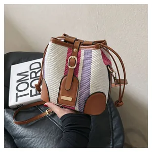 Detail of striped bucket bag featuring cream canvas and brown leather drawstring closure