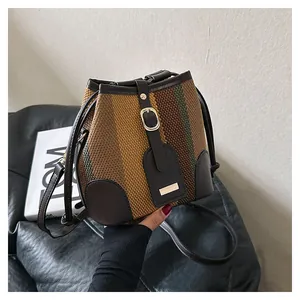 Detailed shot of striped woven bucket bag featuring brown leather trim and metal buckle