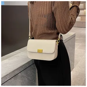Close-up of a cream-white leather shoulder bag with gold metal buckle shown on a model