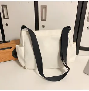 Détail du sac bandoulière en nylon blanc avec sangle noire et poches latérales