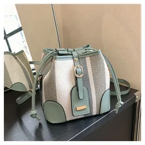 Detail of striped woven bucket bag with green faux leather trim and drawstring closure