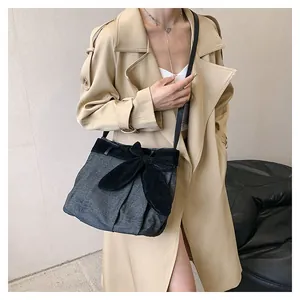 Detail of grey canvas crossbody bag with large black bow and leather shoulder strap