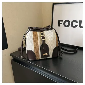 Detailed view of striped woven bucket bag with brown leather trim and golden buckle