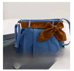 Detail presentation of denim hobo bag with brown suede bow and smartphone for size scale